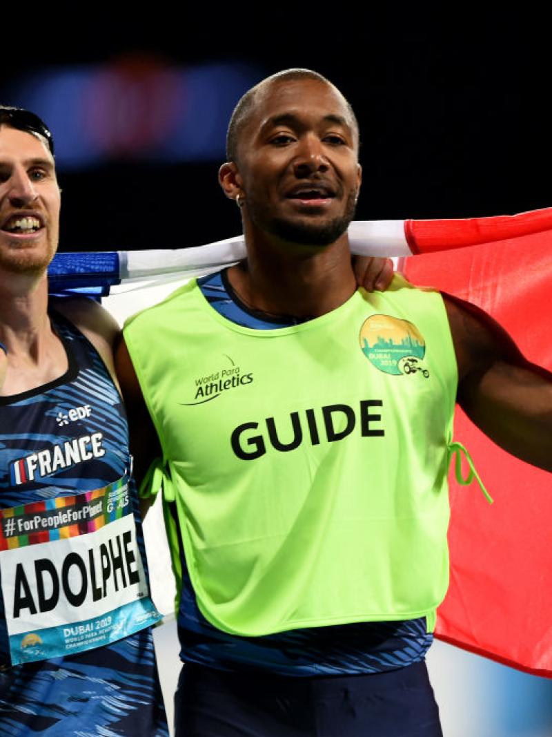 A white vision impaired man and his guide celebrate holding the French flag