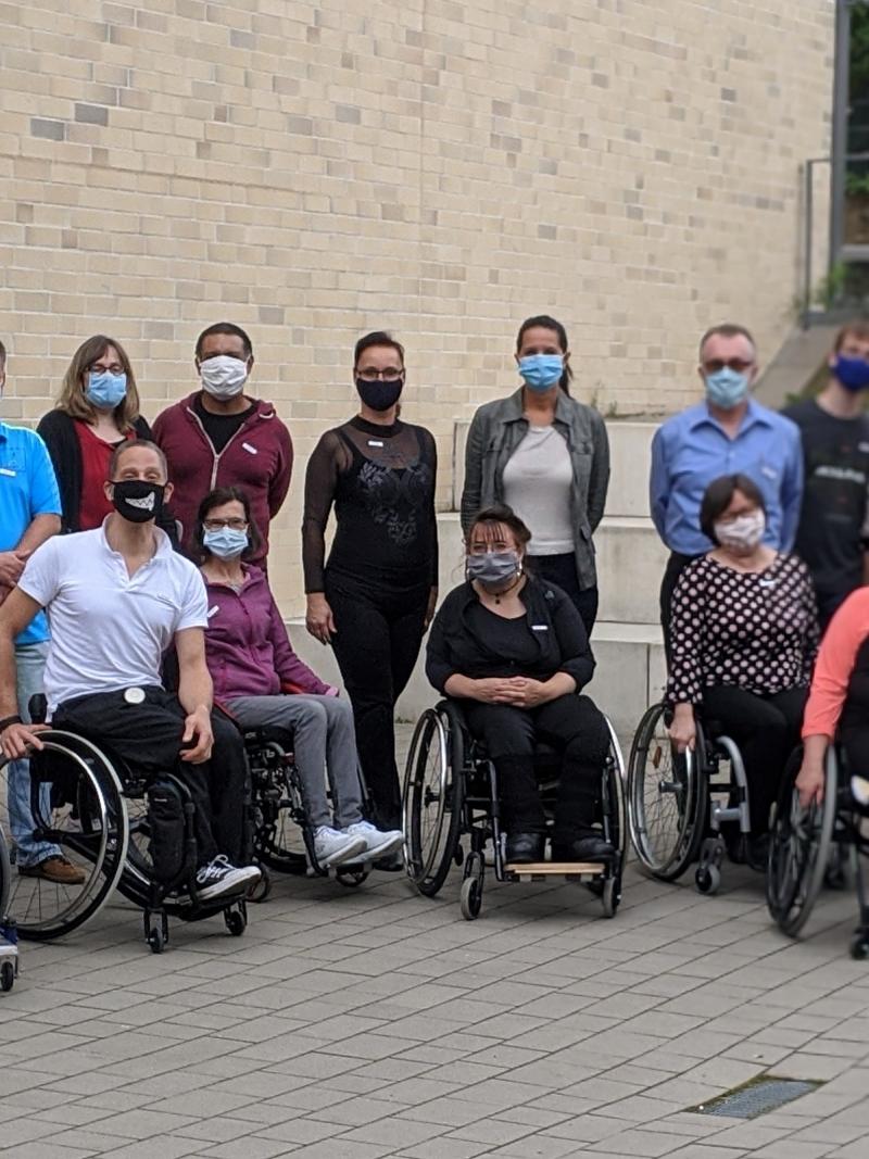 A group of wheelchair users outdoors with a group of standing people behind them