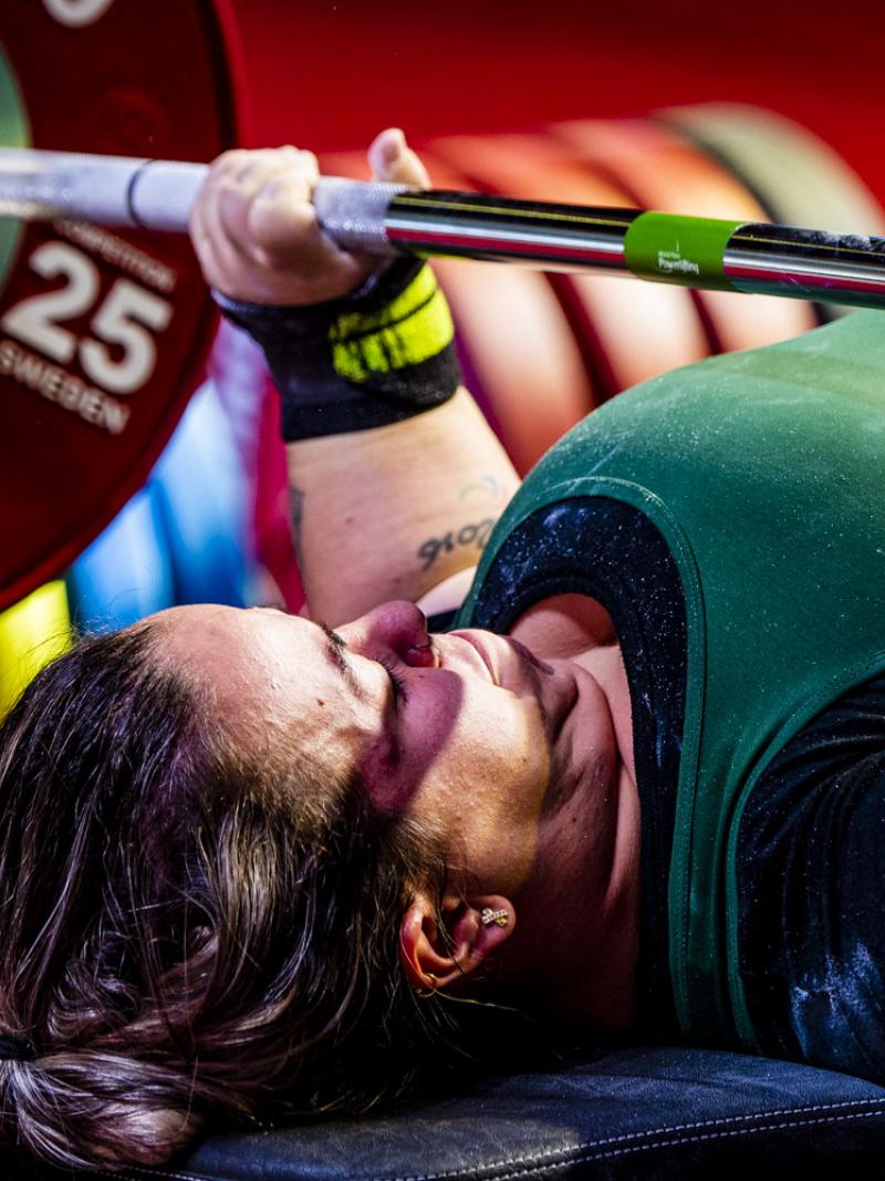 A short-stature woman lifting a bar on a bench press