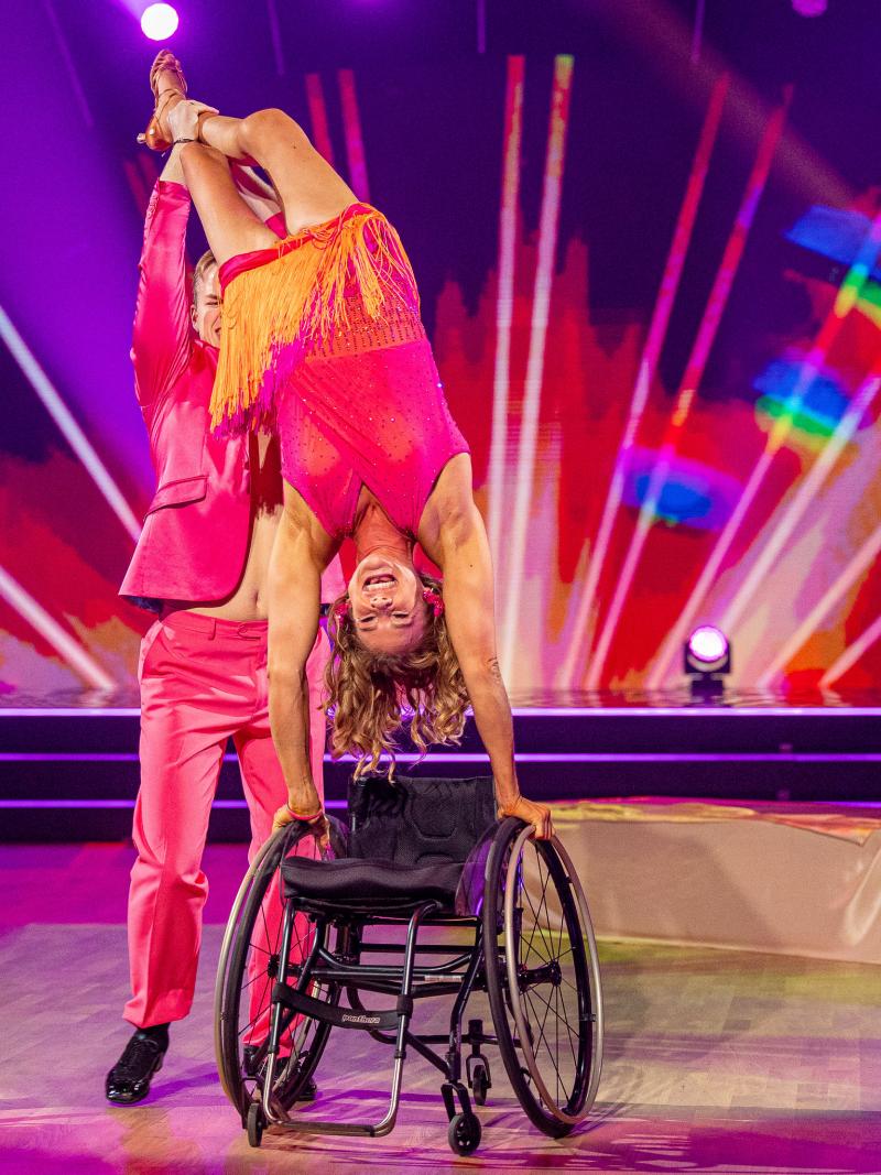 A woman in a wheelchair on a dance floor held by her dance partner