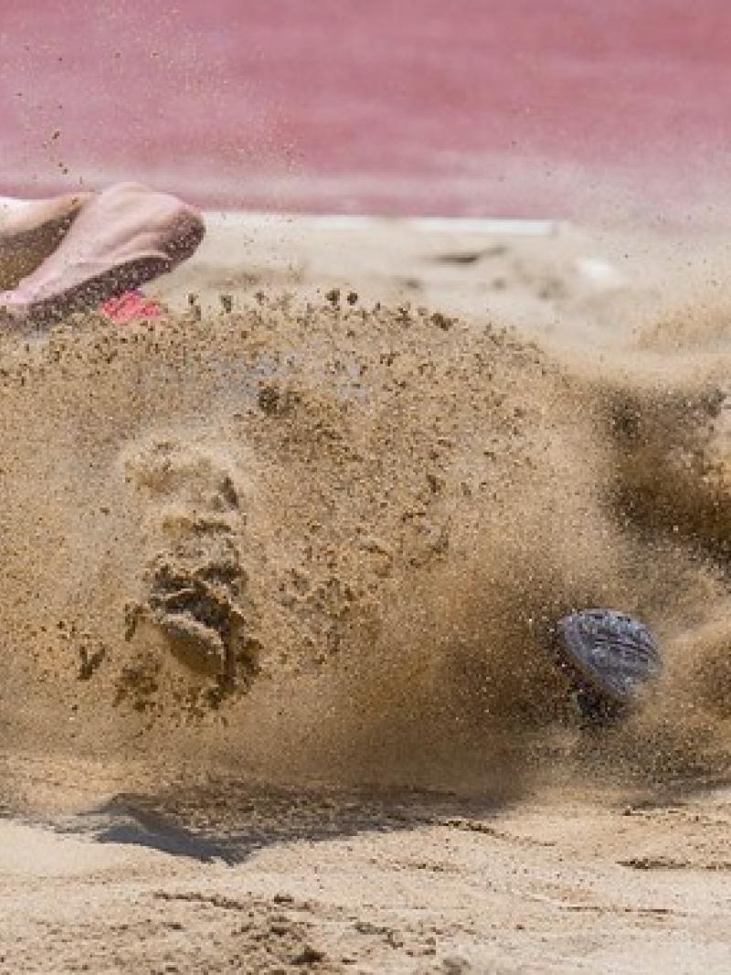 A man with a blindfold landing in a sand pit of a long jump track