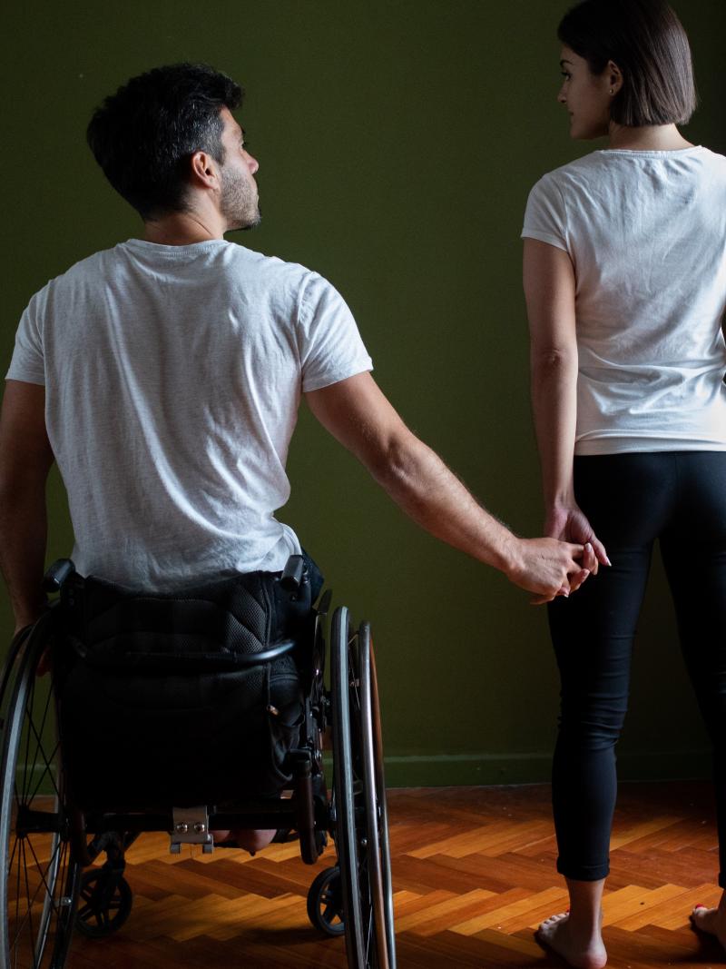 A man in a wheelchair holding the hand of a standing woman