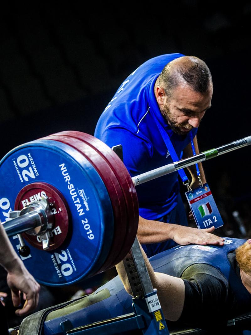 A man on a bench press preparing to lift a bar with three man standing around him