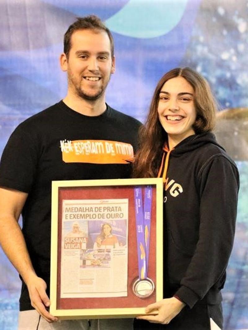 A man and a young woman smiling and holding a frame with a newspaper page and a medal