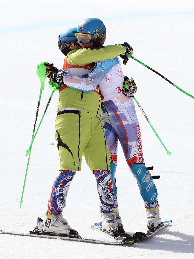 Two male alpine skiers hugging each other on the snow