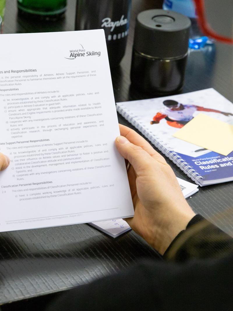 A woman reading a notebook with a World Para Alpine Skiing logo