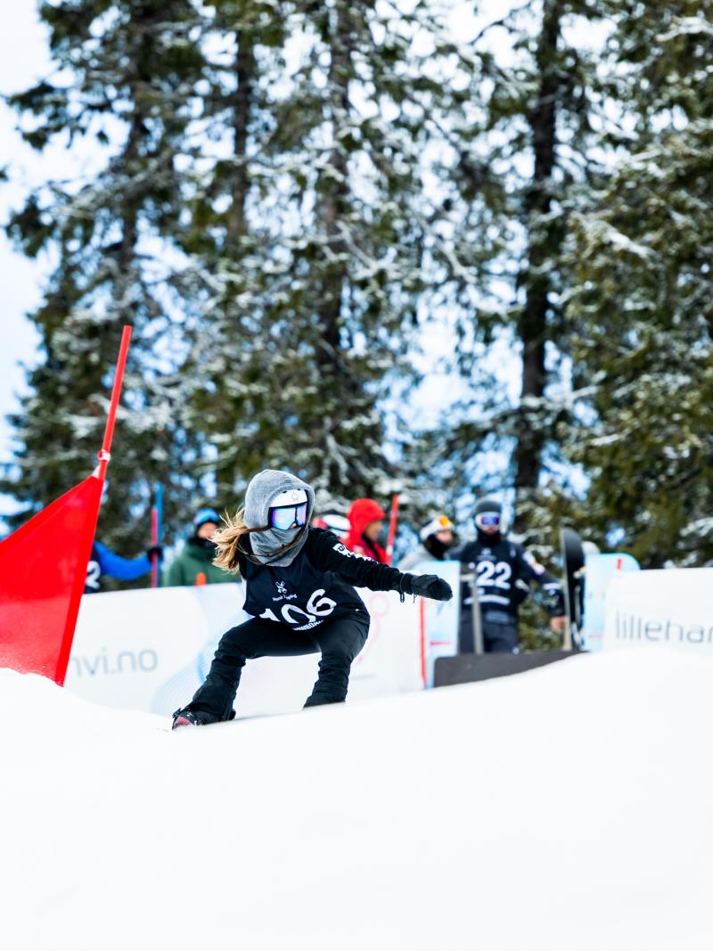 A female snowboarder competing being observed by a group of nine people in the background