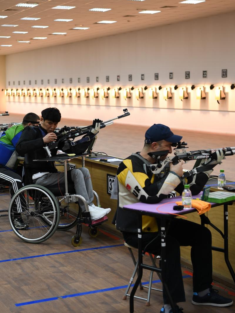 A group of men seated with rifles competing in an indoor shooting range