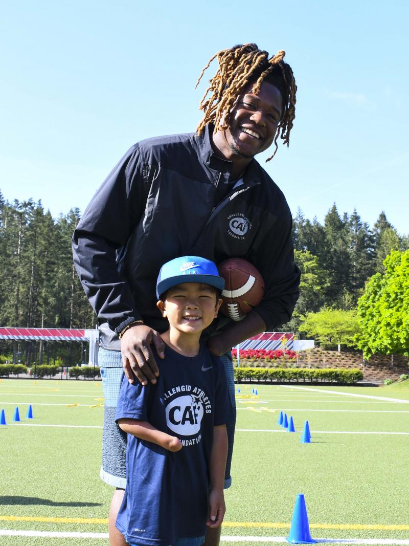 Black male athlete holding an American football and smiling with a kid with an arm impairment