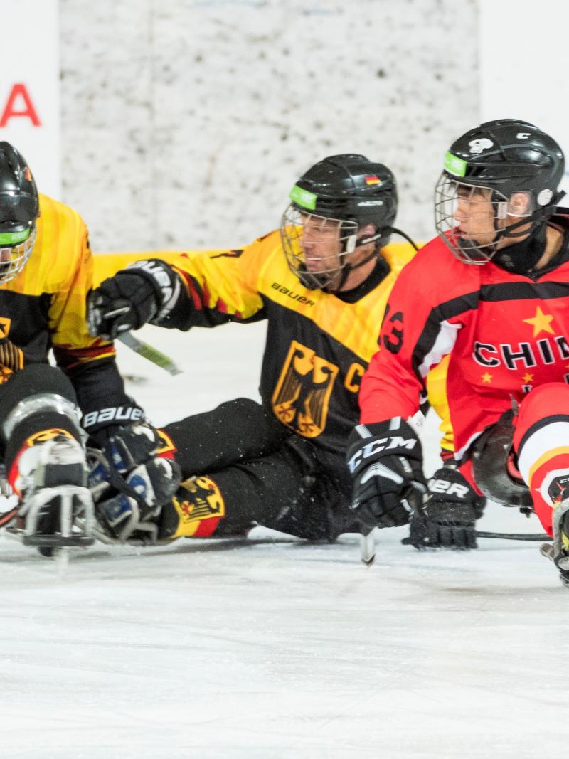 A man with the Chinese uniform on an ice sledge competing against two other men wearing Germany's uniform