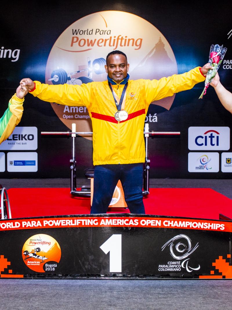 A man standing in the centre of a podium holding the hands of two other men in wheelchairs