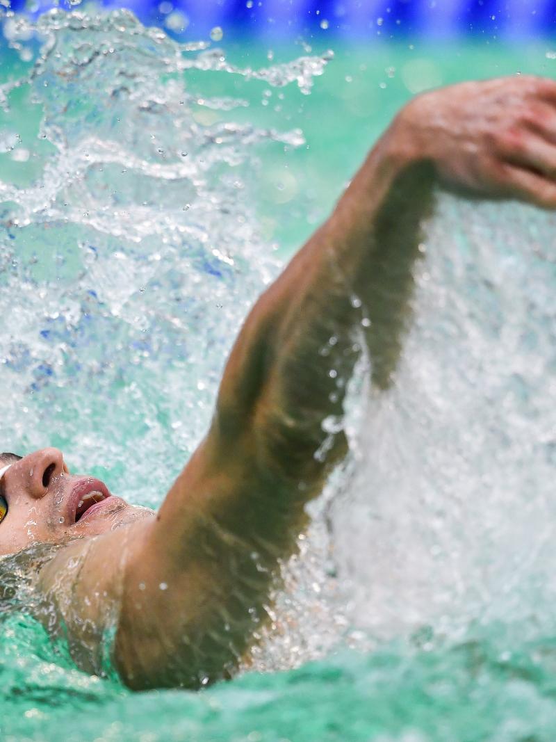 A man with a white cap swimming backstroke in a swimming pool