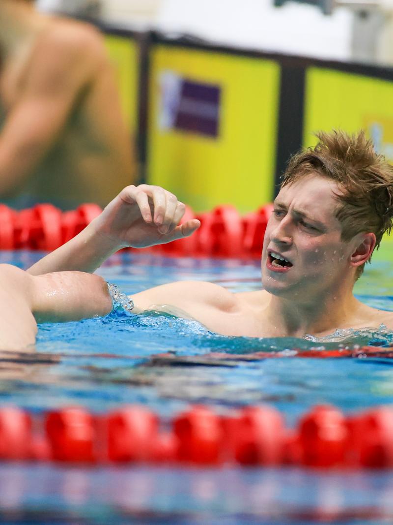 A male swimmer celebrating near another swimmer seeing from behind in a swimming pool