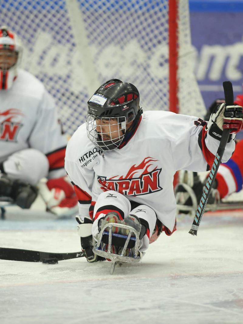 A sledge hockey player from Japan on an ice rink with Japan's goaltender and a Czech Republic player in the background