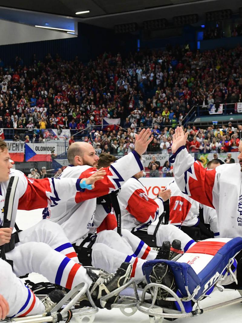One Para ice hockey player giving high five to a group of players on sledges in a crowded ice hockey arena