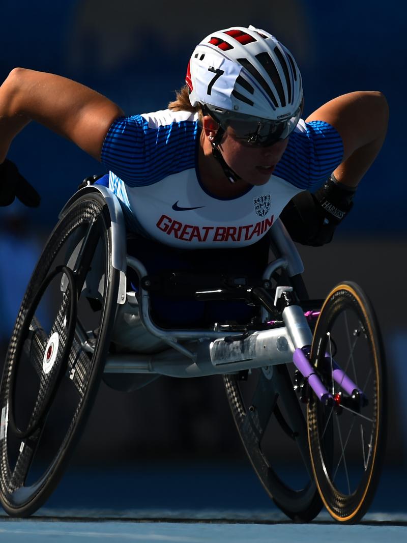 A female athlete competing in a wheelchair race in a blue track