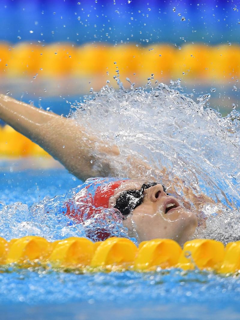 A woman with a red cap swimming backstroke in a pool