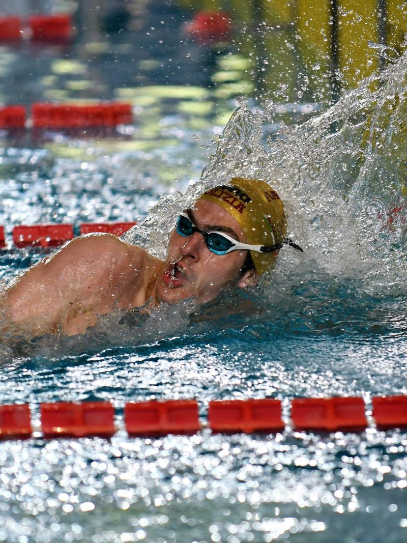 A male swimmer finishing his race in a swimming pool