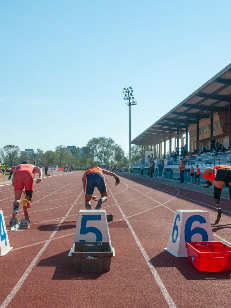 A red athletics track with athletes seeing from behind running from the starting blocks