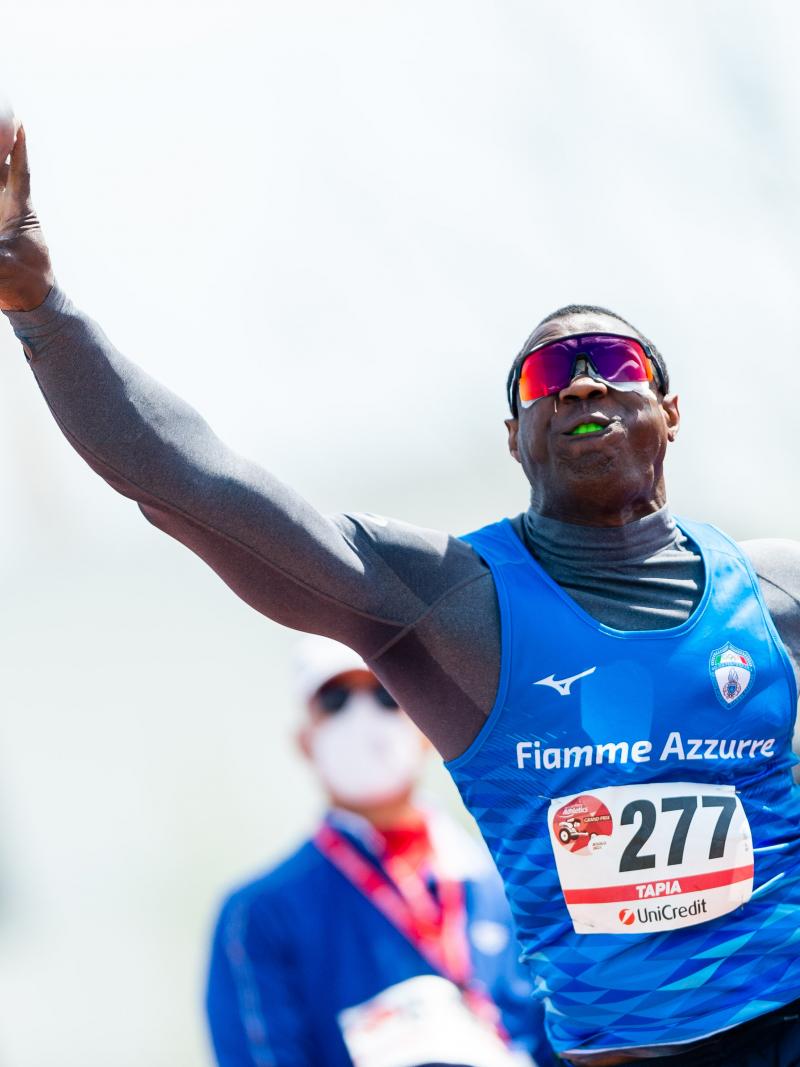 A man competing in shot put observed by another man 