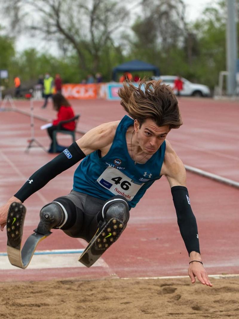 A men with prosthetic legs competing in a long jump event observed by a female official