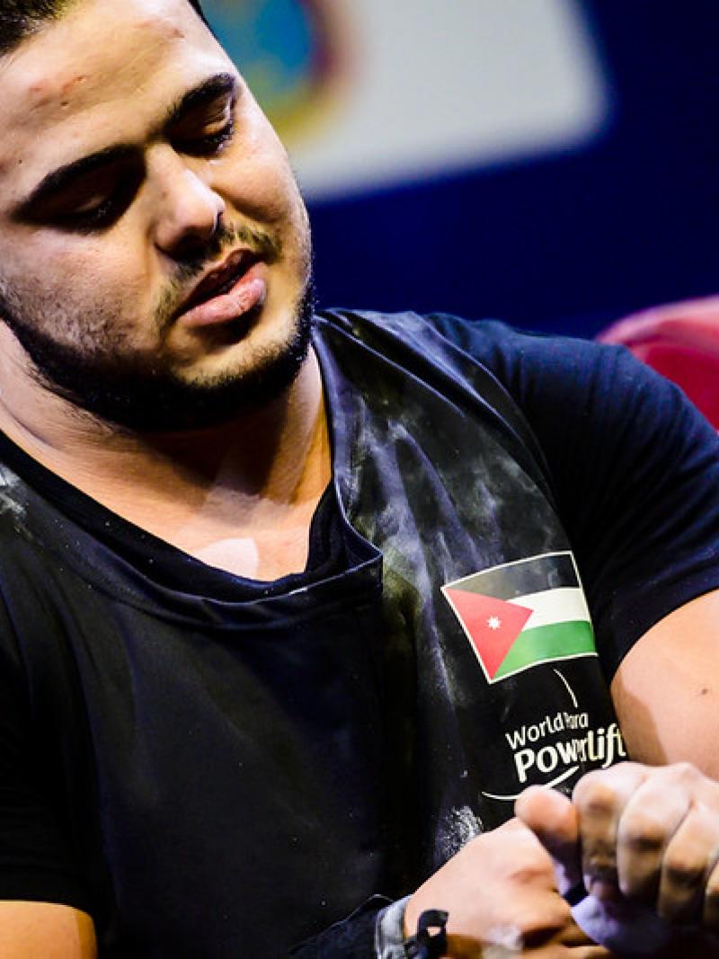 A man in a black shirt looking down to his arms 