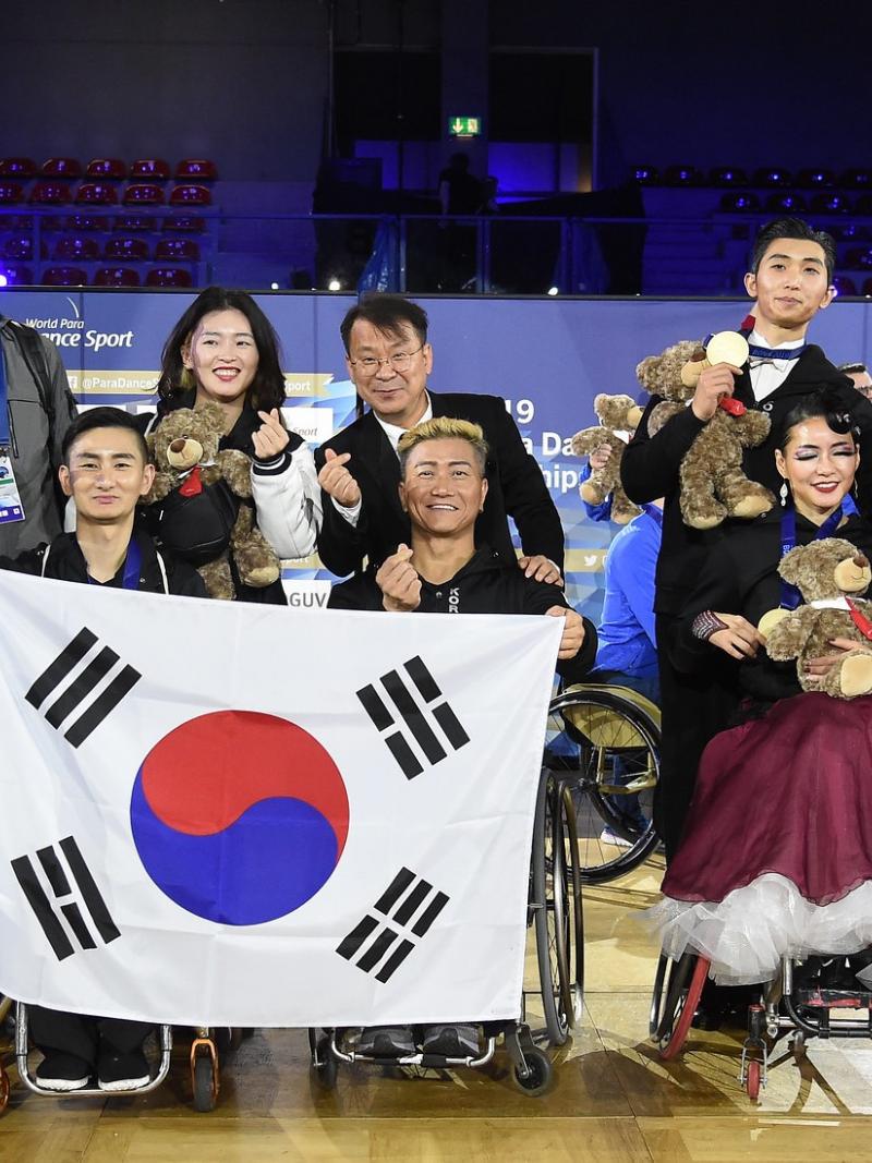 A group of 12 South Koreans, four of them in wheelchairs, posing for a group photo after the Bonn 2019 World Para Dance Sport Championships