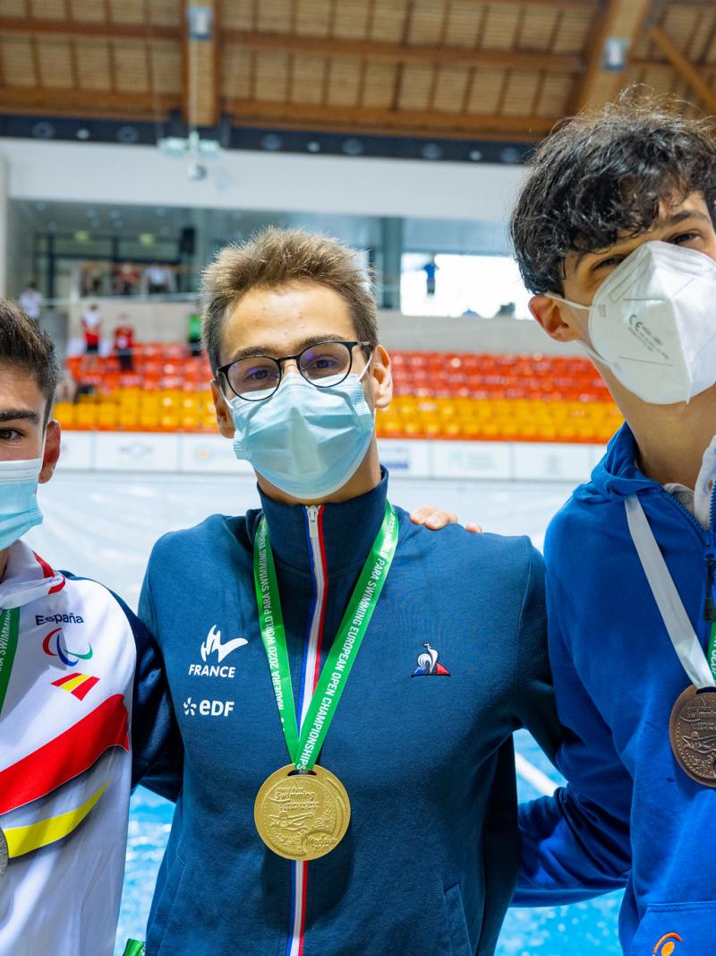 Three men together with their medals in front of a swimming pool