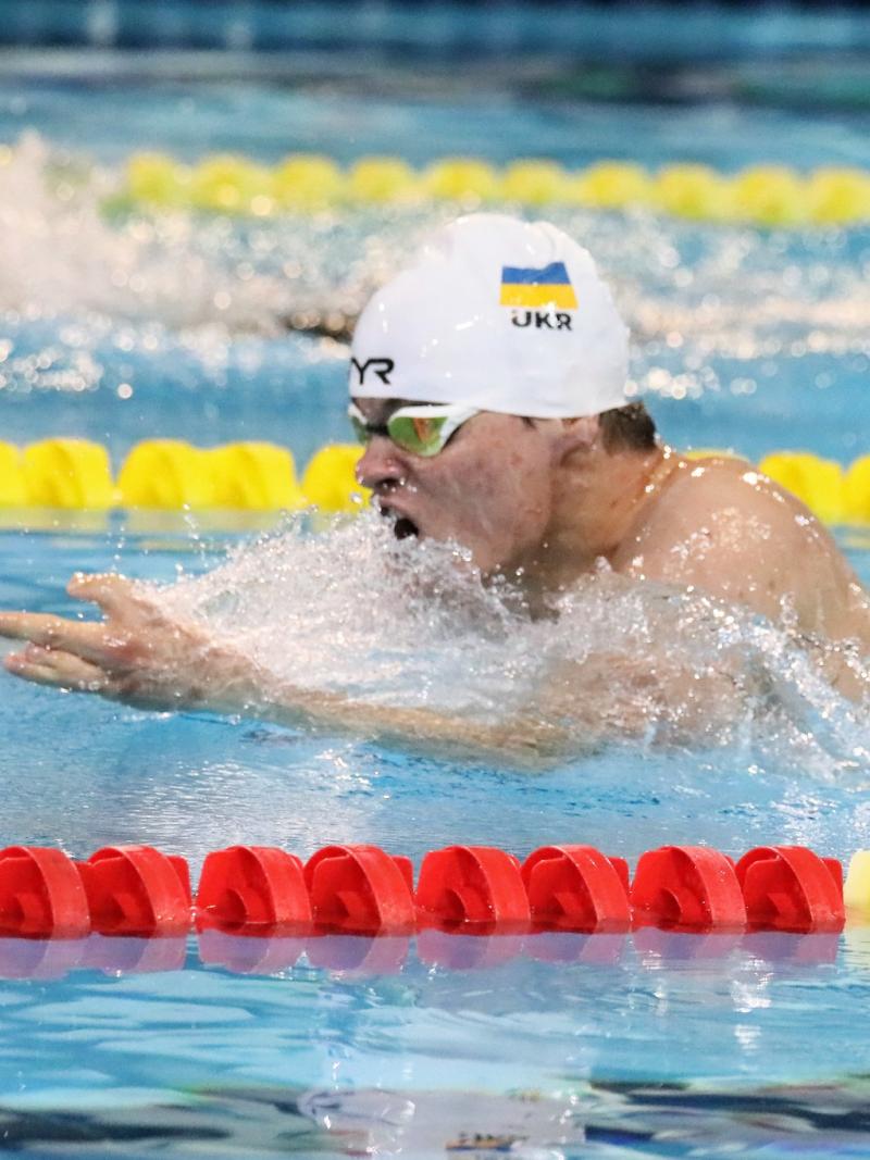 A man with a white cap and the Ukrainian flag swimming breaststroke in a pool