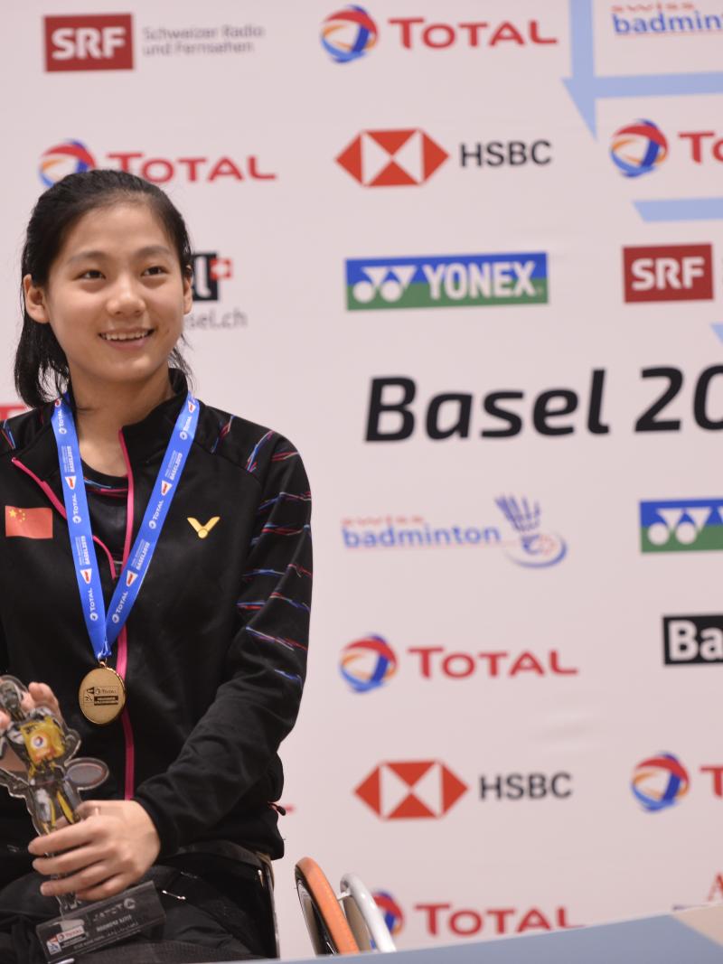 Chinese badminton player Liu Yutong smiles while holding a trophy on the podium