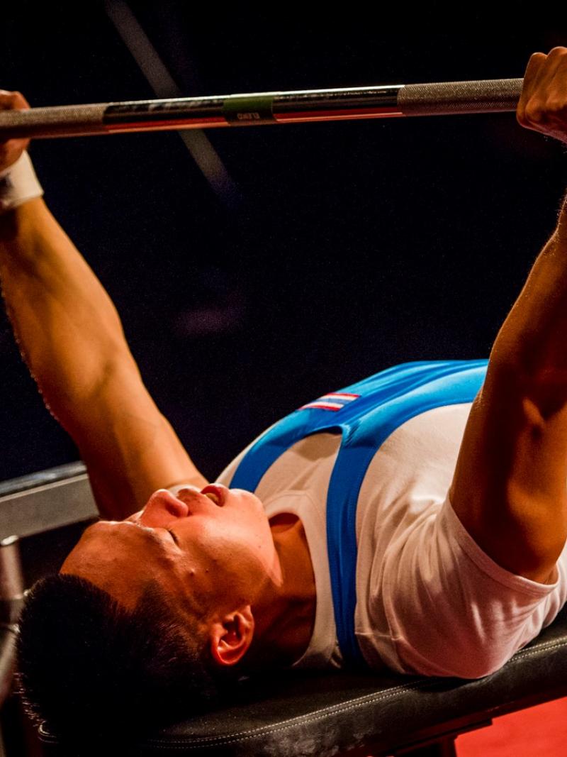 A man on a bench press lifting a bar in a Para powerlifting competition