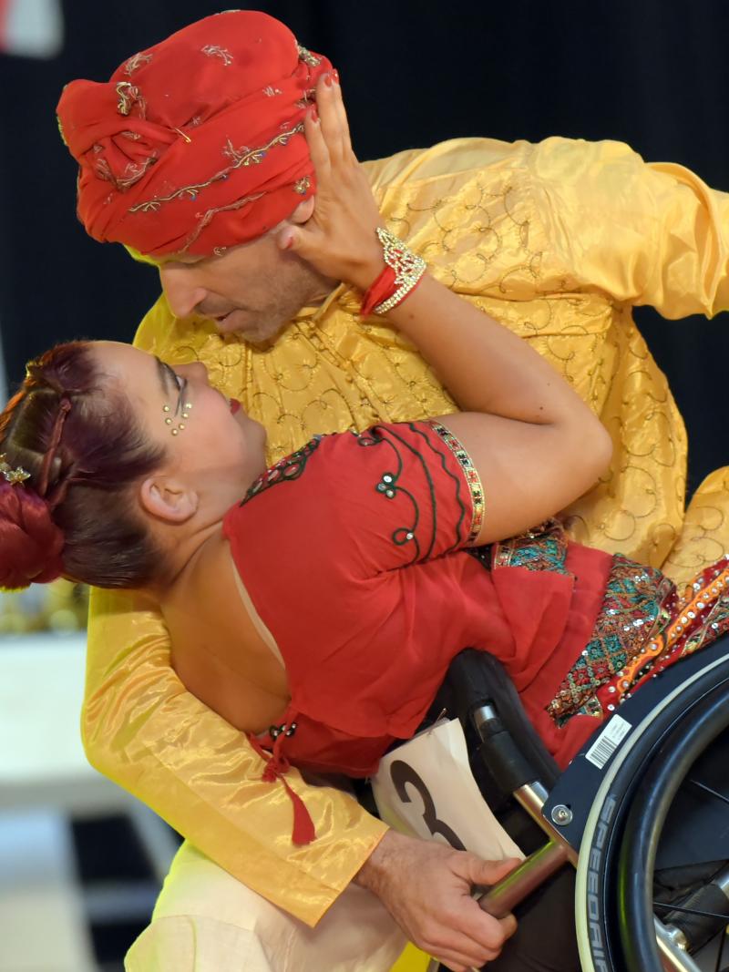 A male standing dancer holding a wheelchair with a female Para dancer during a competition