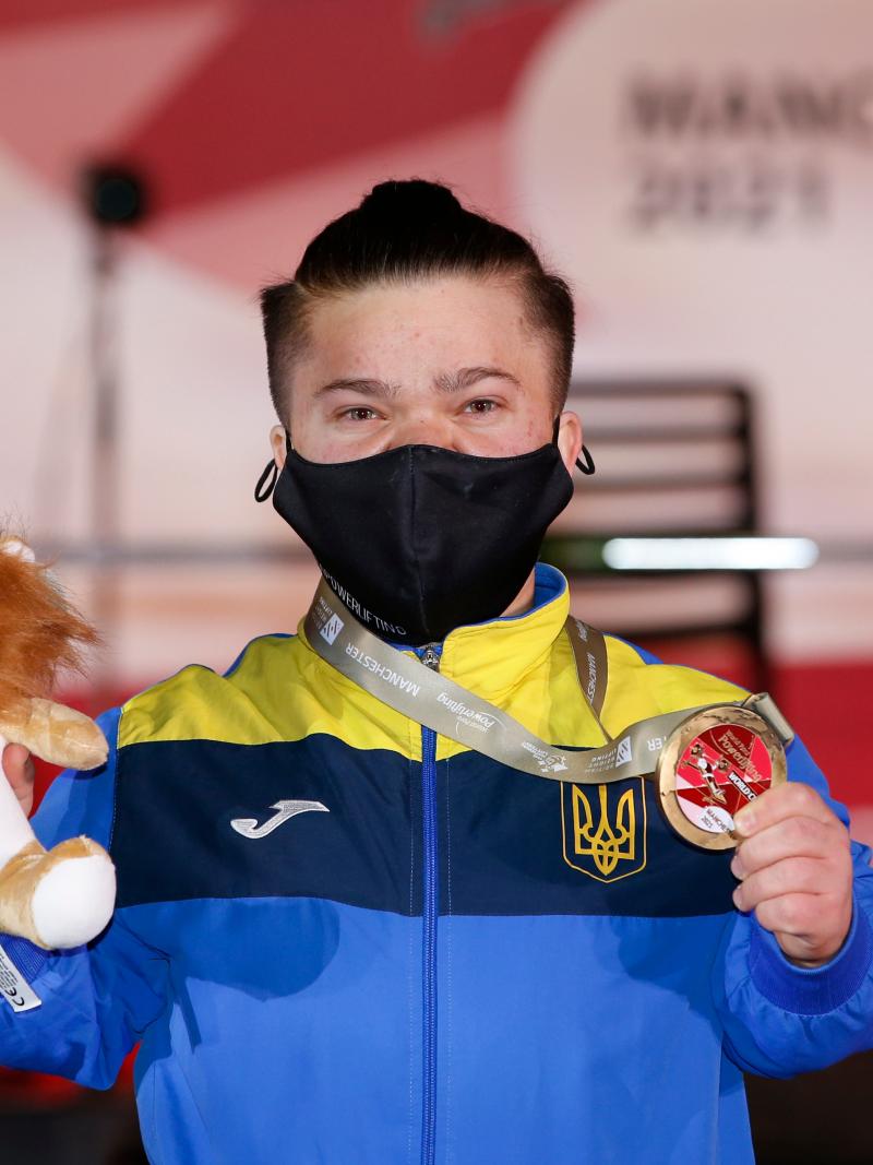 A woman with a face mask showing a medal and a Teddy bear mascot