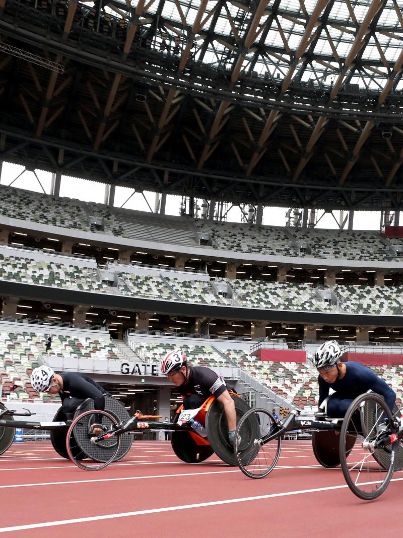 A group of five male wheelchair racers on an athletics track in an empty stadium