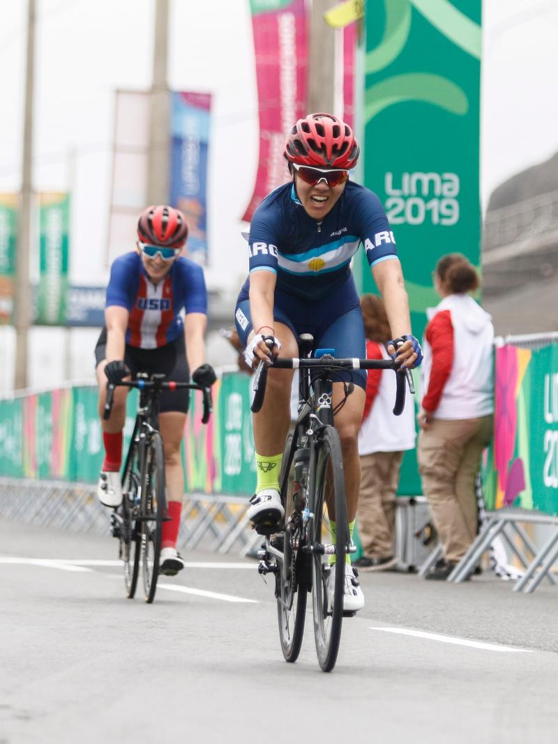 Argentine cyclists smiles after crossing the road race finish line first as Colombian cyclist who came second smiles to her