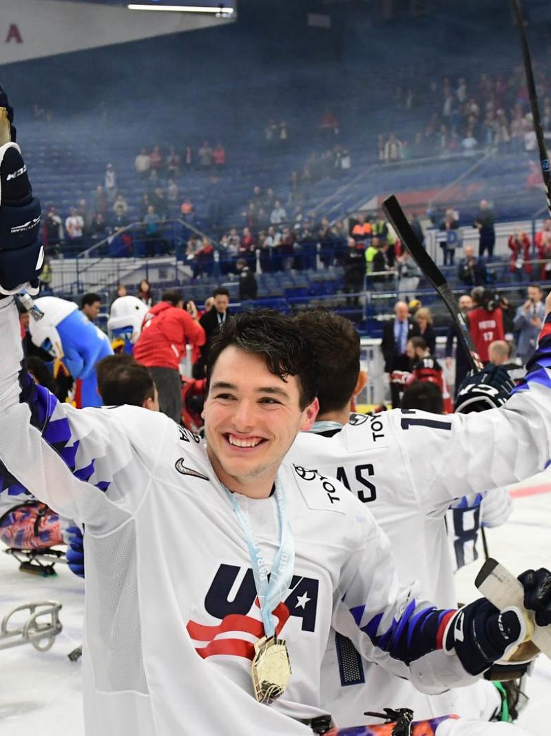 A man celebrating with a group of Para ice hockey players on an ice rink after a match in an indoor arena