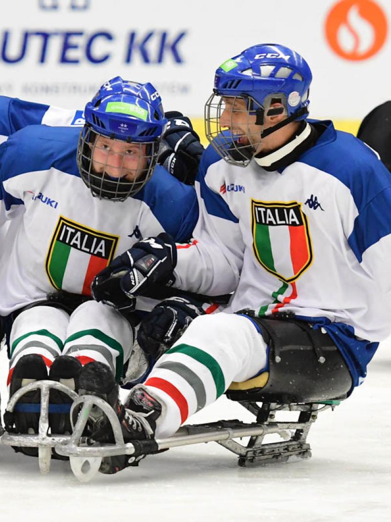 Three Para ice hockey players with the uniform of Italy celebrating with another player from Japan observing