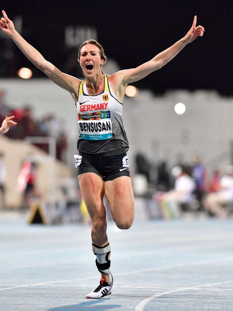 A female athlete celebrating after finishing a race ahead of two other women with prosthetic legs