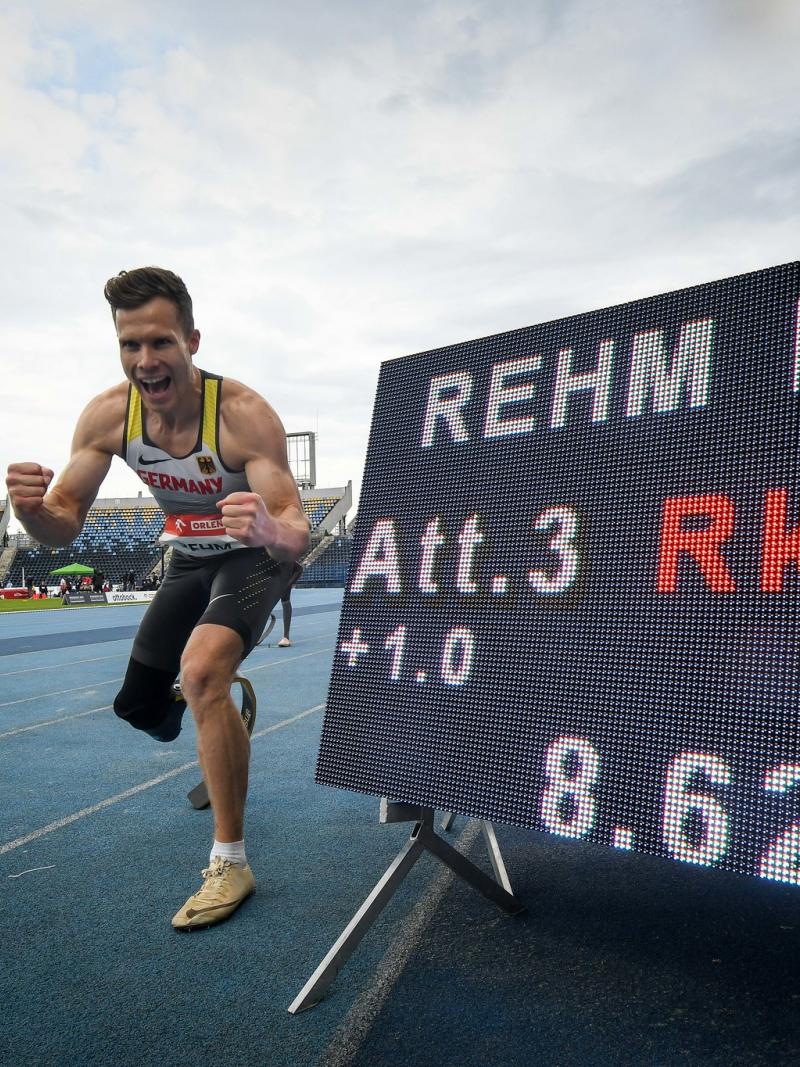 A man with a prosthetic leg celebrating in an athletics track next to a screen showing his world record result