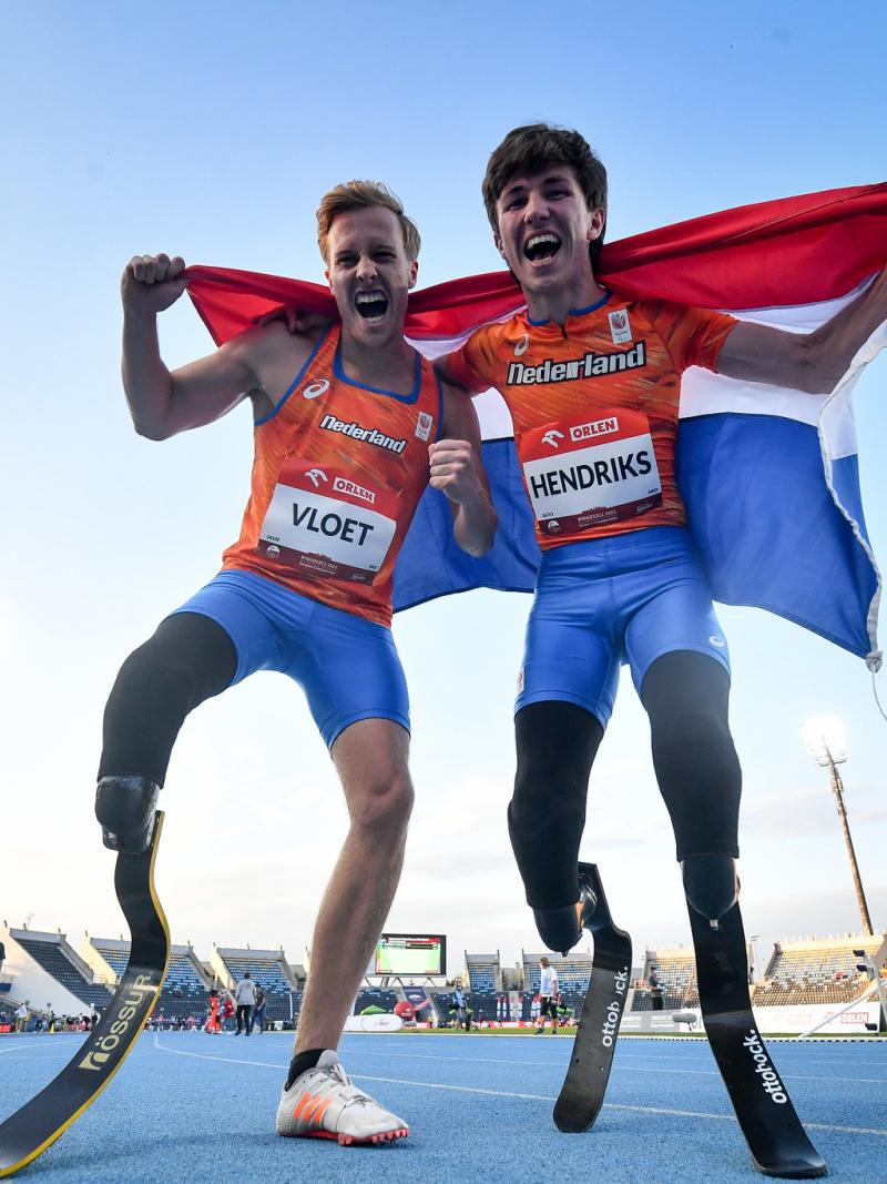 Two male sprinters with prosthetic legs celebrating with the flag of Netherlands
