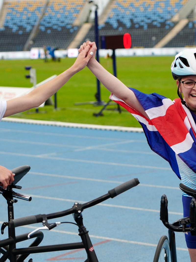 Two young women holding hands on an athletics track