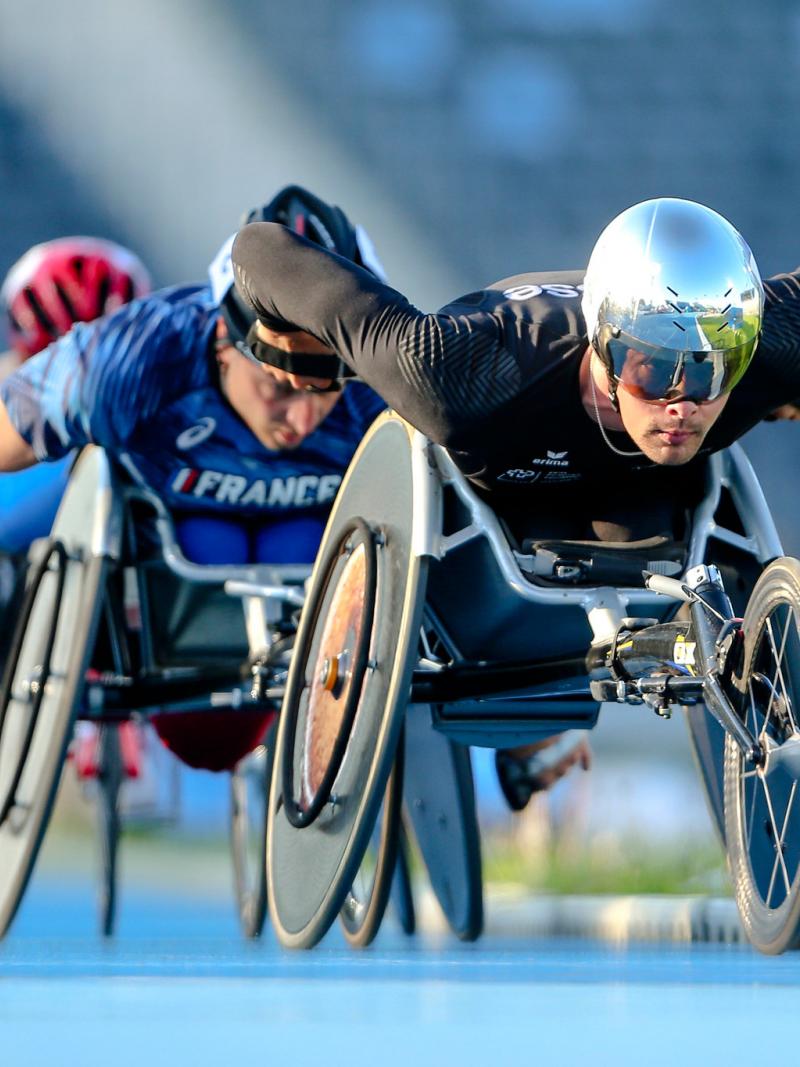 A men in a racing wheelchair leading a competition being followed by two competitors