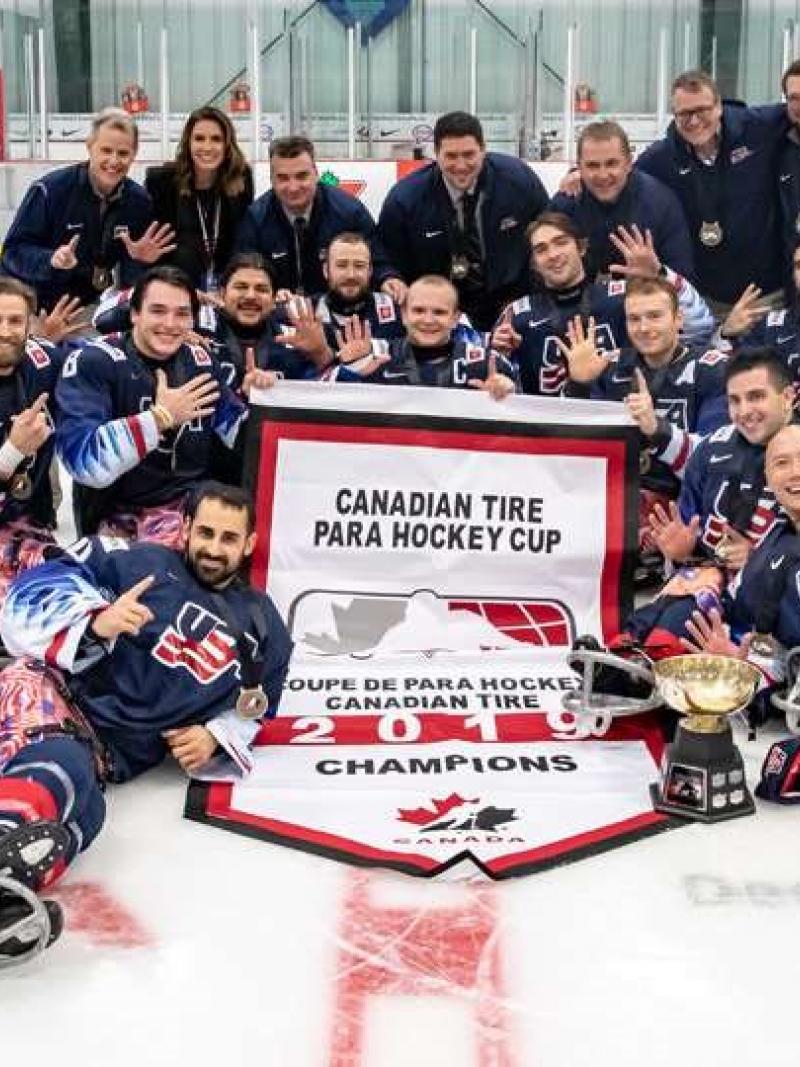 The USA Para ice hockey team posing for picture with a trophy on an ice rink