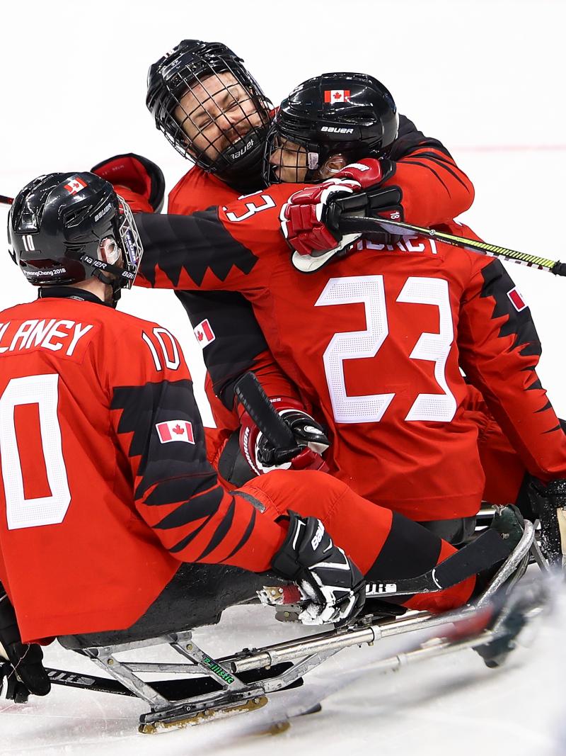 Three Canadian Para ice hockey players hugging in celebration during a game