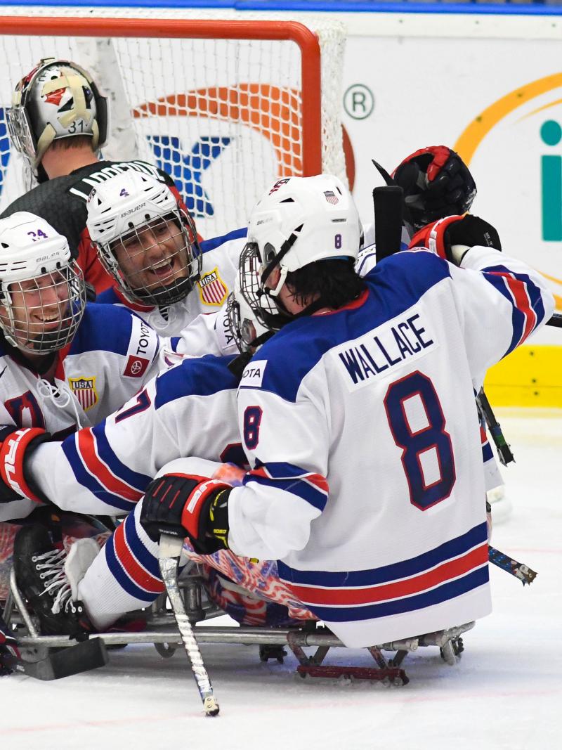 Three USA Para ice hockey players hugging during a game on an ice rink
