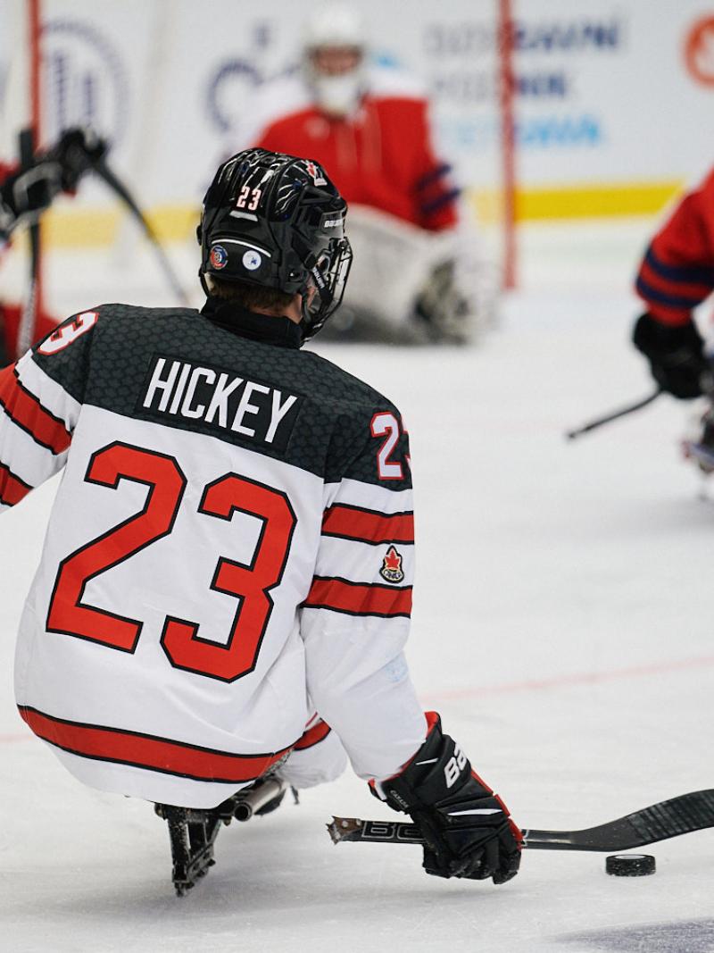 A Para ice hockey player seen from behind in a match observed by three players