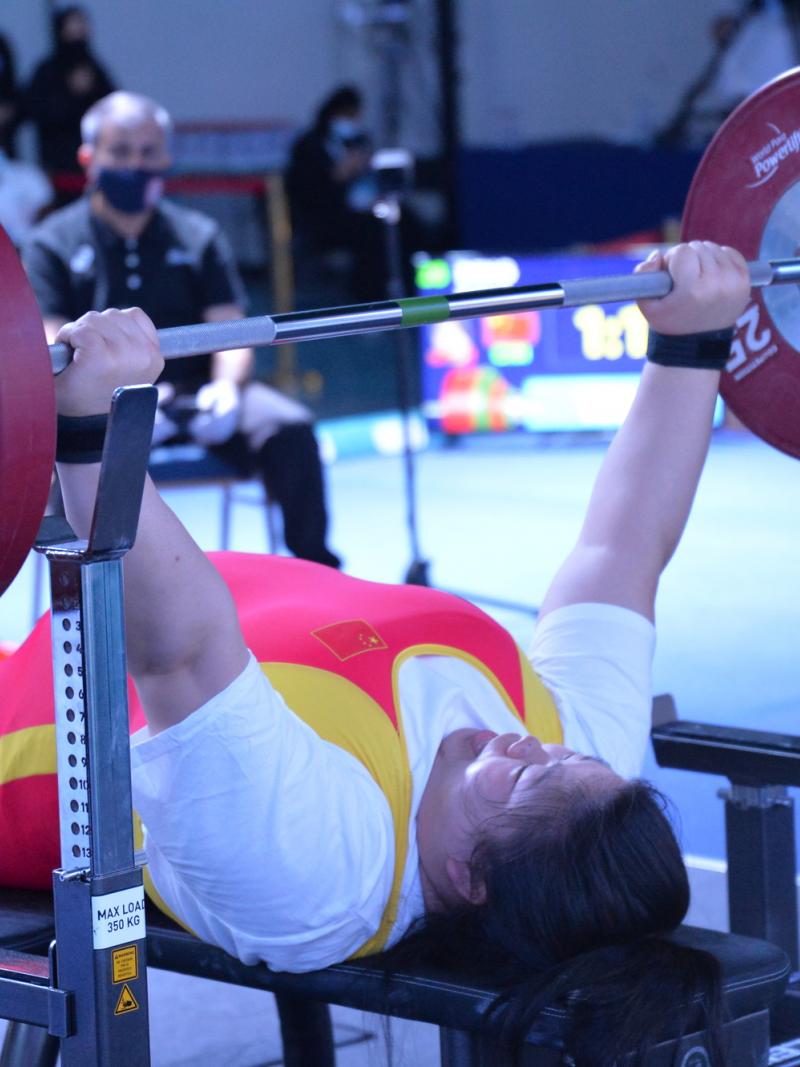 A female powerlifter making a lift observed by a group of people during a competition