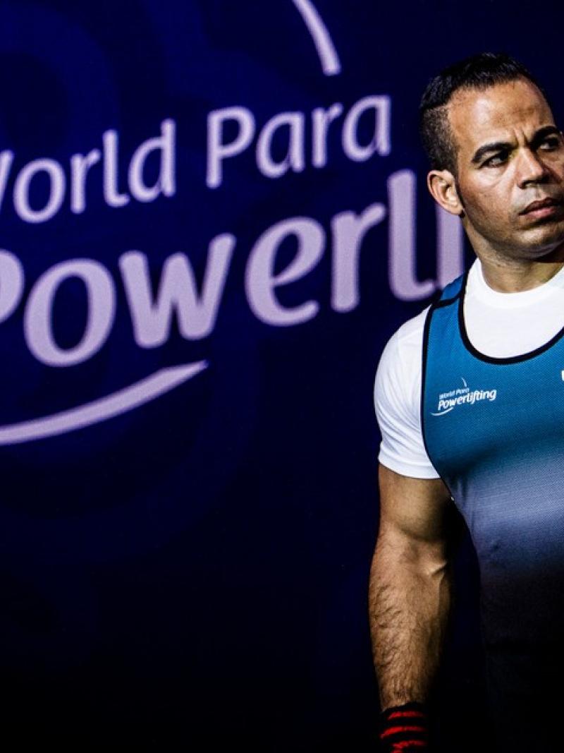A man walking on a stage with a logo of World Para Powerlfiting in the background
