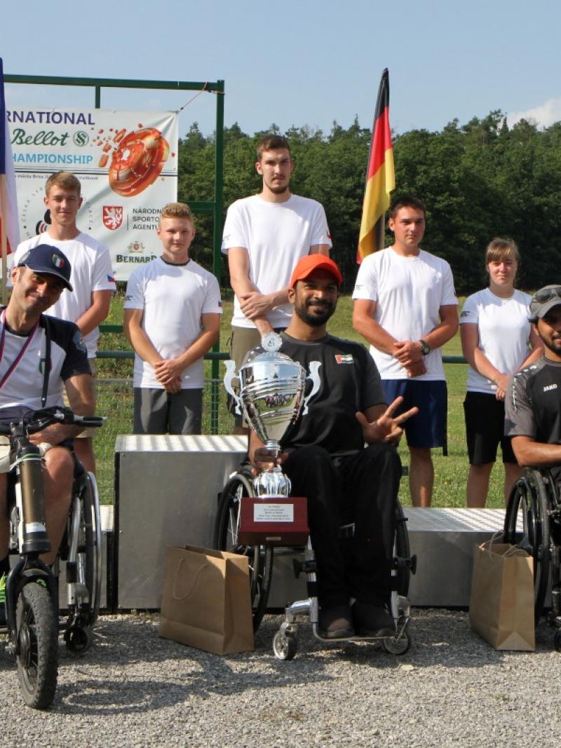 Three men in wheelchairs holding trophies with seven persons standing behind them