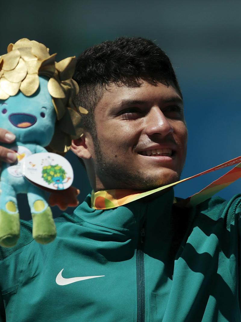 A man without an arm holding a mascot and showing his gold medal